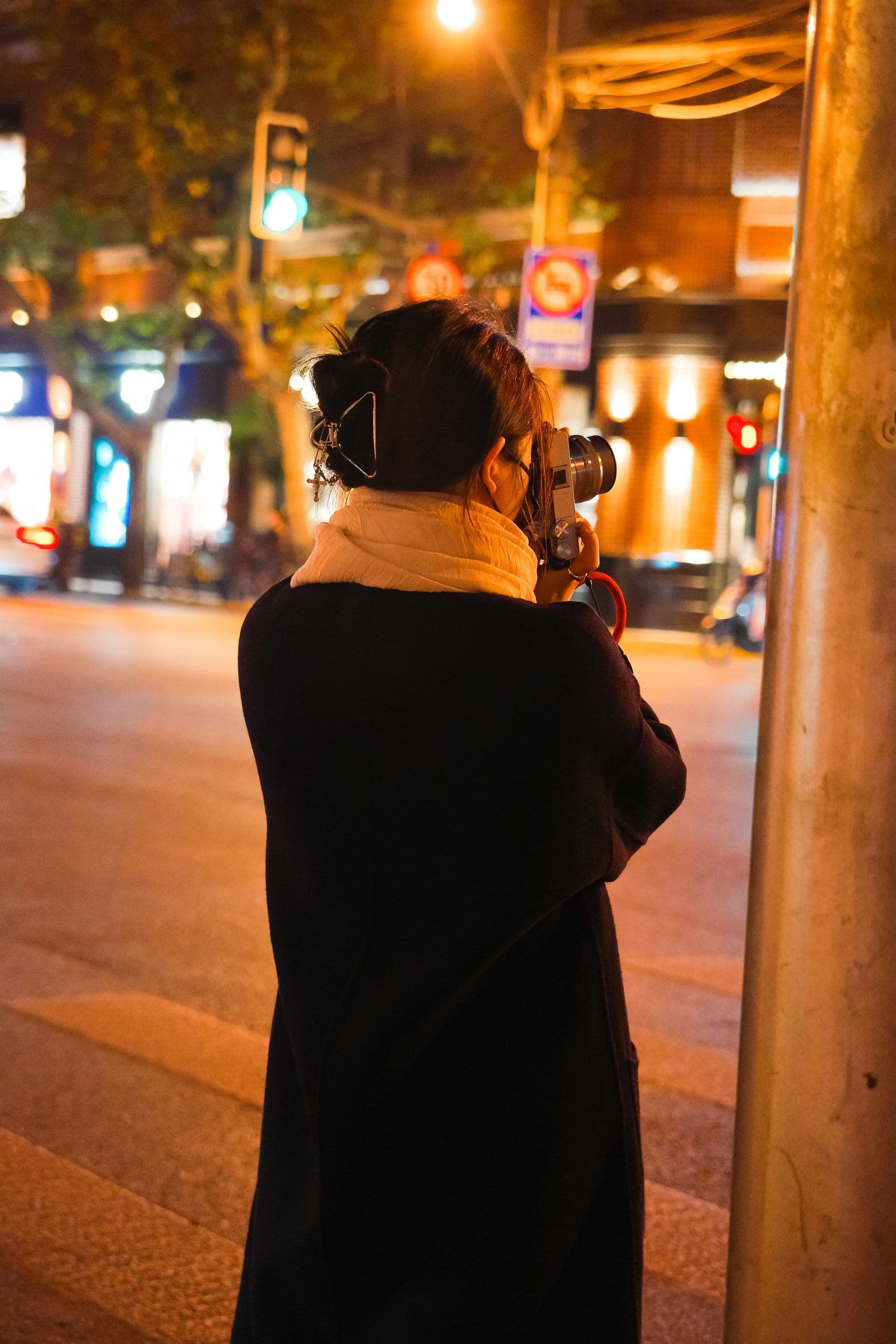 A person photographing an evening street in Shanghai, seen from behind in warm city light
